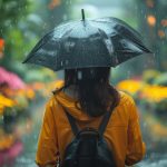 Person in a yellow raincoat holding a black umbrella, standing in a rainy garden filled with colorful flowers and soft glowing lights, symbolizing quiet resilience and reflection.