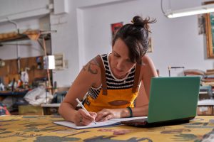 Woman working in home environment, taking notes near a laptop