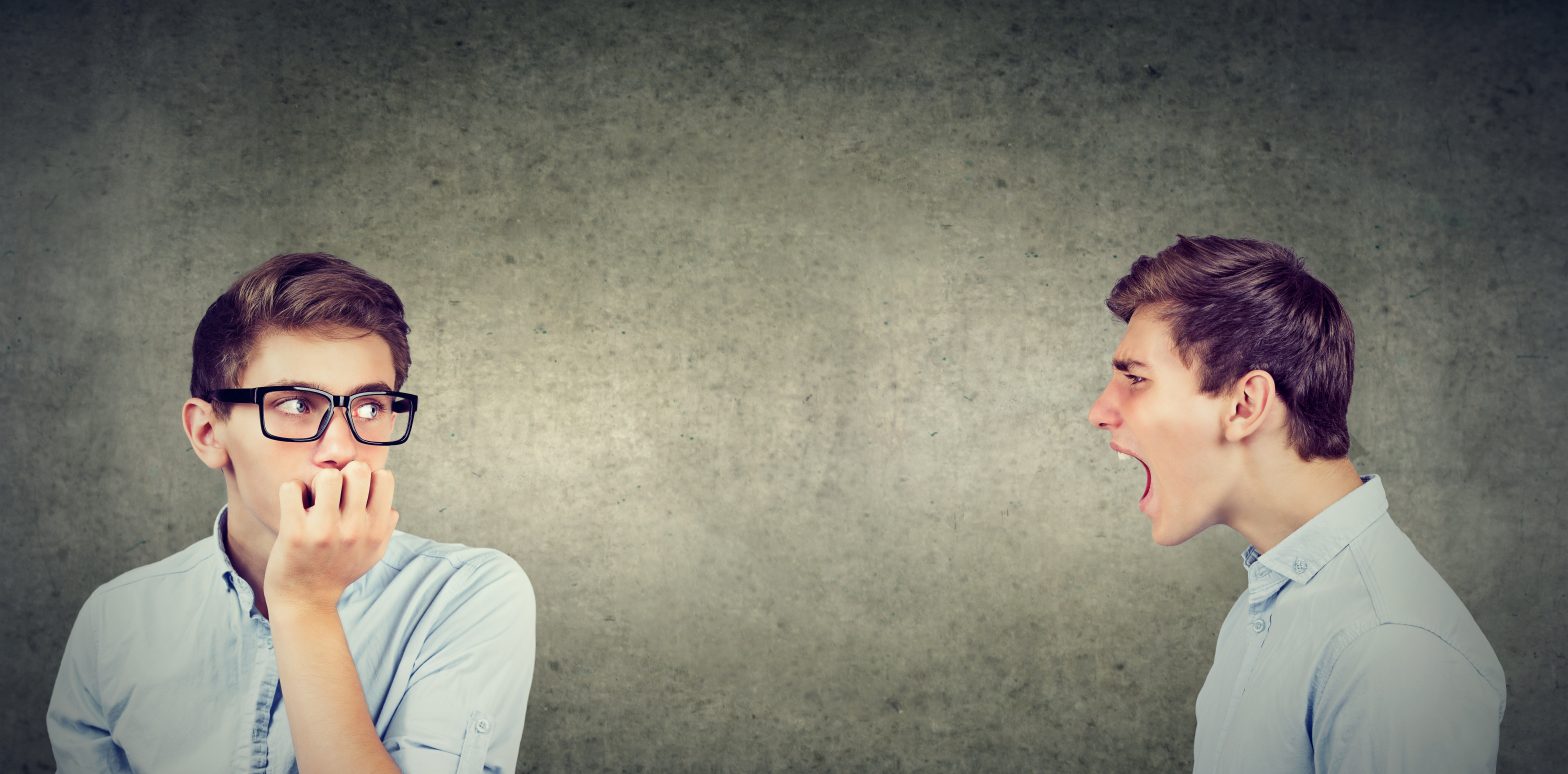 Anxious man in glasses listening to angry, critical version of himself scream at him.