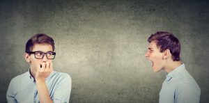 Anxious man in glasses listening to angry, critical version of himself scream at him.