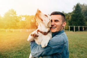Happy young man holding dog Labrador in hands at sunset outdoors