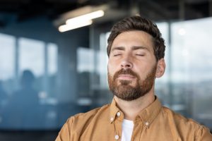 Man indoors with eyes closed, taking a slow breath, appearing calm and grounded.