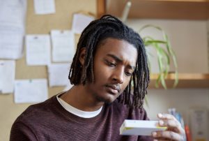 Young man sitting at a desk, carefully reading the packaging of a medication.