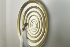 Woman standing in front of concentric circular shapes resembling a tunnel or repeating loop, symbolizing overthinking, mental patterns, and repetitive thought cycles.