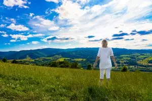 Woman standing in an open grassy landscape overlooking mountains and sky, symbolizing mental clarity, spaciousness, and relief from overthinking.