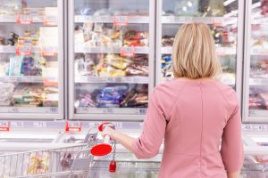 Woman standing still in front of grocery store freezer shelves filled with choices, symbolizing overthinking, decision fatigue, and mental loops.