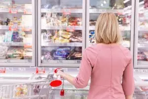 Woman standing still in front of grocery store freezer shelves filled with choices, symbolizing overthinking, decision fatigue, and mental loops.