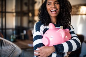 Smiling woman hugging a piggy bank, representing the affordability and long-term value of at-home ketamine therapy.