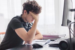 Person sitting at a desk with head in hand, feeling overwhelmed while avoiding a work task, illustrating avoidance behavior.