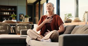 Woman practicing deep breathing at home, demonstrating a simple way to regulate your nervous system and reduce stress.