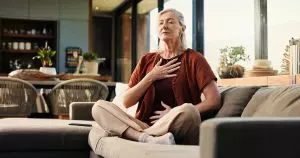 Woman practicing deep breathing at home, demonstrating a simple way to regulate your nervous system and reduce stress.
