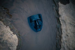 Dark blue theatrical mask partially submerged in murky water, symbolizing conflict avoidance, self-silencing, and losing touch with one's authentic voice.