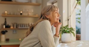 Woman gazing out a bright window in a warm home setting, appearing peaceful, present, and at ease in an ordinary moment of daily life.