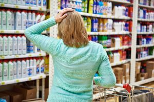 Person standing in a store aisle with a hand on their head, appearing overwhelmed by a simple purchasing decision, illustrating the decision fatigue and hesitation often associated with functional freeze.