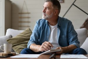 Man sitting on a sofa with a notebook in hand, pausing to reflect in a quiet moment at home, representing self-awareness, presence, and personal growth.