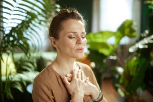 Person with eyes closed and hands resting on their chest in a calm indoor setting, illustrating grounding, nervous system regulation, and a growing sense of safety.