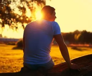 Person sitting outdoors at sunset, reflecting quietly as the nervous system settles and recovers from chronic stress over time.