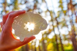A hand holds a brain-shaped puzzle with a missing center piece as sunlight shines through the opening, symbolizing new perspective, self-awareness, and challenging limiting beliefs.