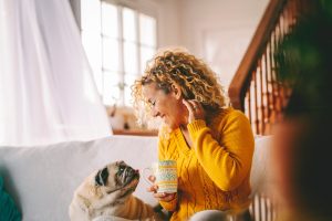 Woman relaxes on the sofa at home while engaging with her beloved pug, showing how low-dose ketamine therapy supports reinforcing daily well-being and emotional balance in daily life.