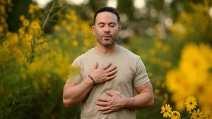 Founder practicing mindful breathing outdoors with one hand on his chest and one on his abdomen, representing the process of building a healthier relationship with yourself through presence and self-awareness.