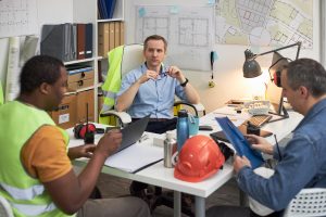 Three men in meeting, engineers with hard hats, calmly discussing their project. 
