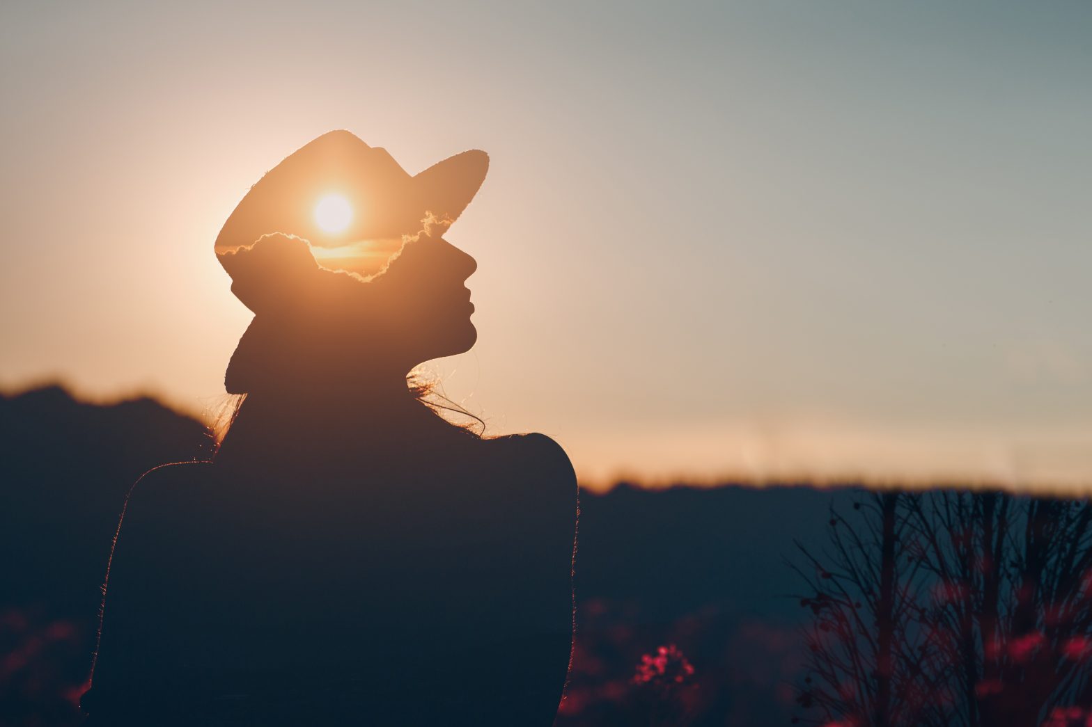 Silhouette of a woman standing outdoors at sunset with sunlight shining through her cap, representing the benefits of regulating the nervous system.