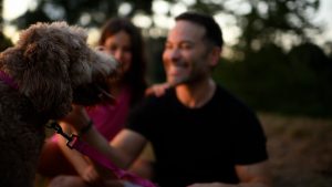 Soft focus photo of a man and his daughter playing with a dog outside.