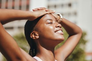 Woman with her hands on her head smiling outside in the sun. Success with ketamine dose in at-home therapy.