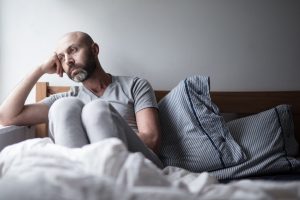A man sitting in bed resting his head on his hand, lost in overthinking, feeling down, illustrating the link between glutamate and depression.