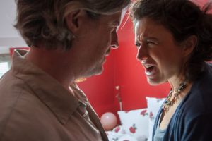 Woman shouting in mans face in red-walled bedroom, representing angry outbursts associated with trauma patterns lodged in the nervous system.