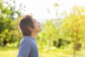 Young man taking a deep breath outside, trees in background, representing repeated experiences of safety that help the nervous system reset for trauma healing.