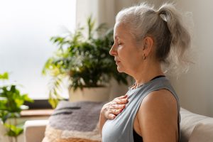 A woman practices a breathing technique to build emotional capacity in a sunlit room with a green plant in the background.