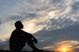 Silhouette of a seated man experiencing ketamine therapy benefits, feeling peaceful and calm at sunset under beautiful clouds in the evening sky.