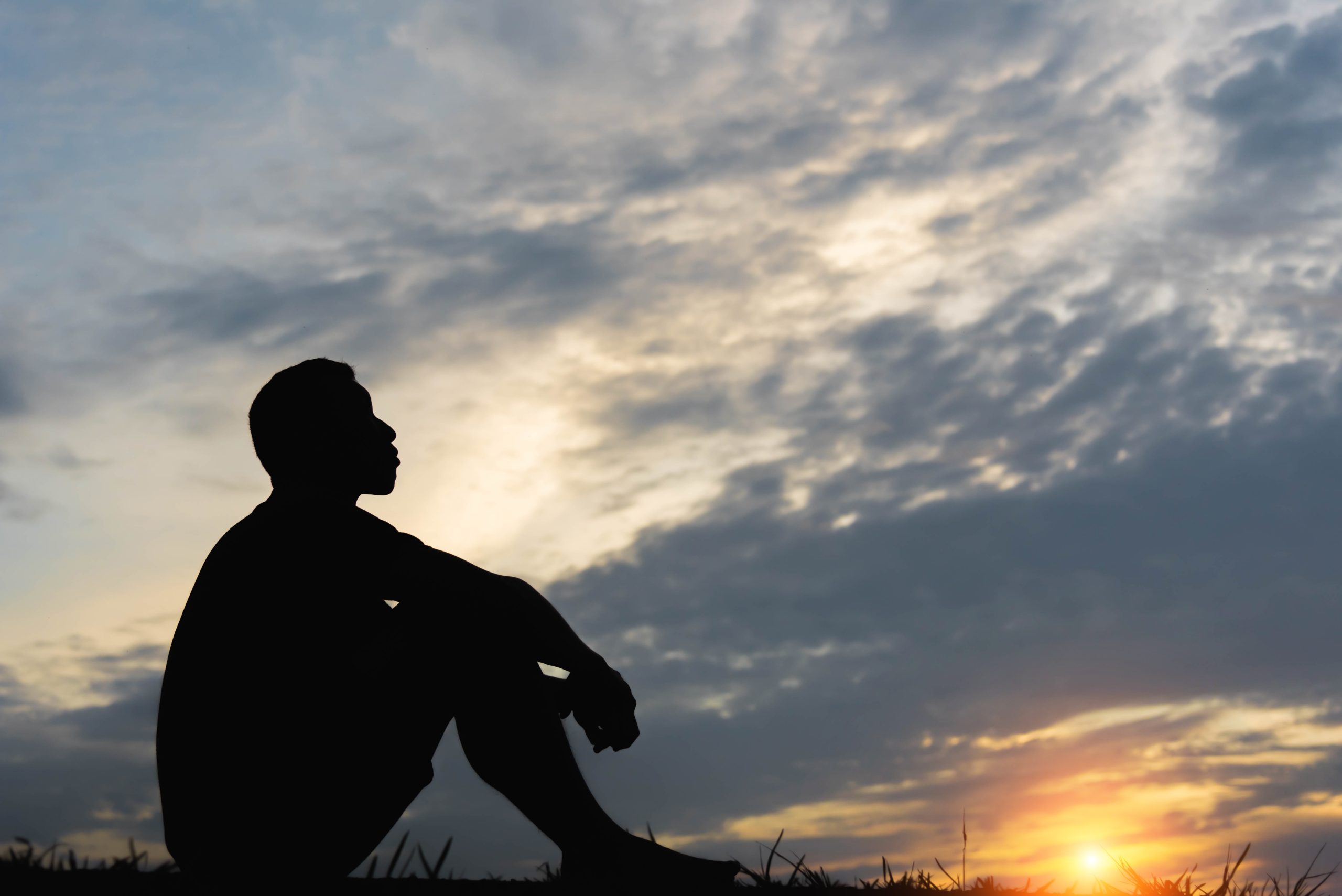 Silhouette of a seated man experiencing ketamine therapy benefits, feeling peaceful and calm at sunset under beautiful clouds in the evening sky.