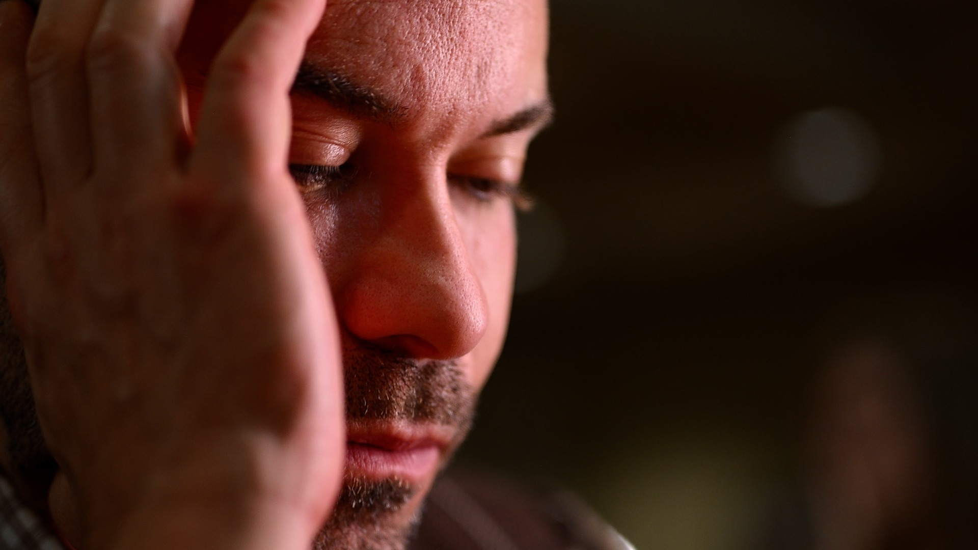 Close up of a man looking down, one hand near his face, feeling broken and hopeless.